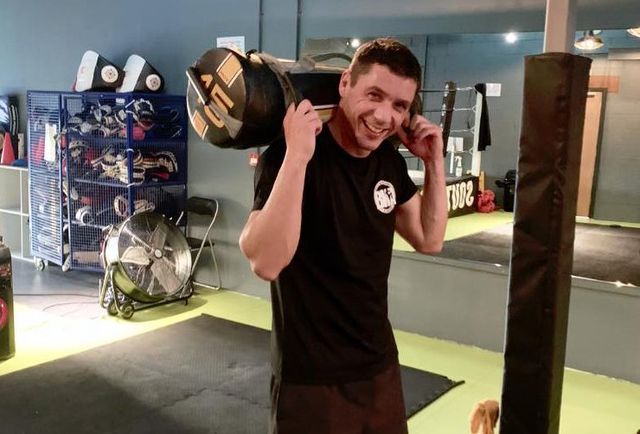 A personal training client grinning with a sandbag across his shoulders in the PT area at South Coast Gym
